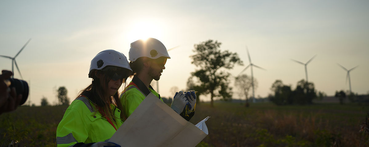 Profissionais com capacetes e coletes de segurança revisam plantas em um parque eólico ao pôr do sol, ilustrando o planejamento técnico para PGRS.