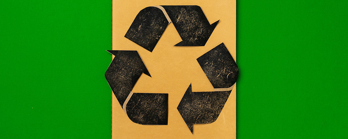 Símbolo de reciclagem preto estampado em caderno marrom sobre fundo verde — veja as principais perguntas e respostas sobre reciclagem.