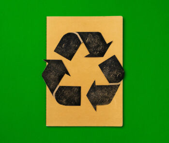 Símbolo de reciclagem preto estampado em caderno marrom sobre fundo verde — veja as principais perguntas e respostas sobre reciclagem.